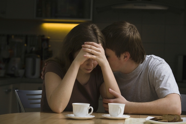 Young man consoling woman at dining table in house