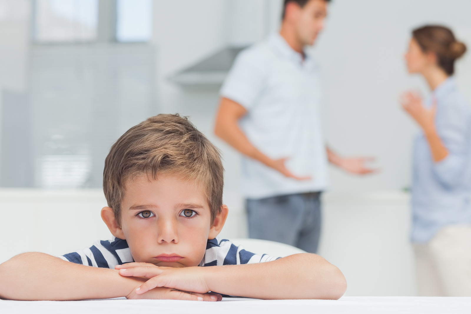 Sad boy with arms folded while parents quarreling in the kitchen